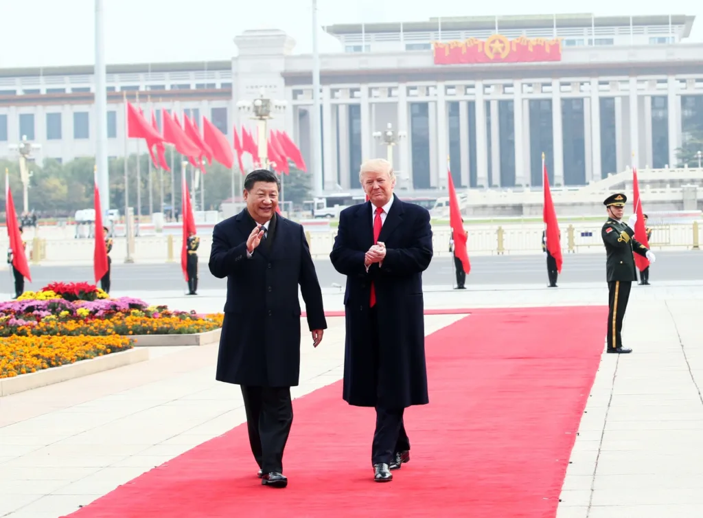 US President Donald Trump and Chinese President Xi Jinping walking together on a red carpet in front of the Great Hall of the People in Beijing during a state visit.