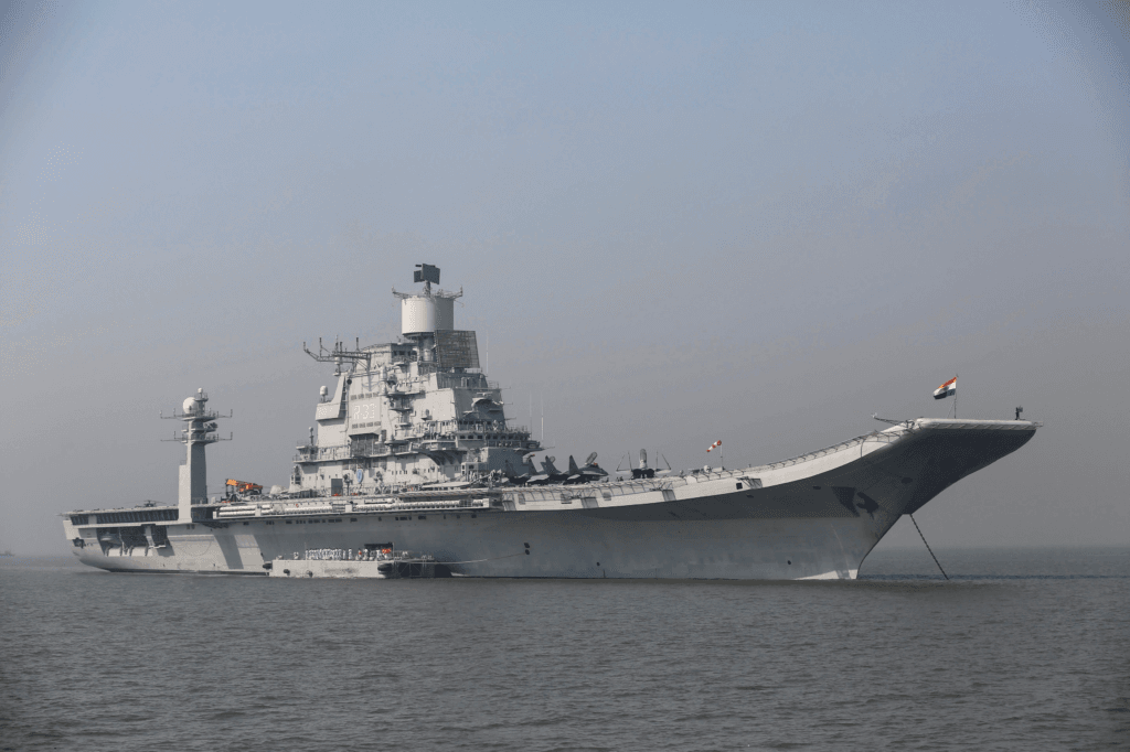 An Indian Navy warship sailing alongside a carrier strike group in the open waters of the Indian Ocean, illustrating the maritime competition between India and China.